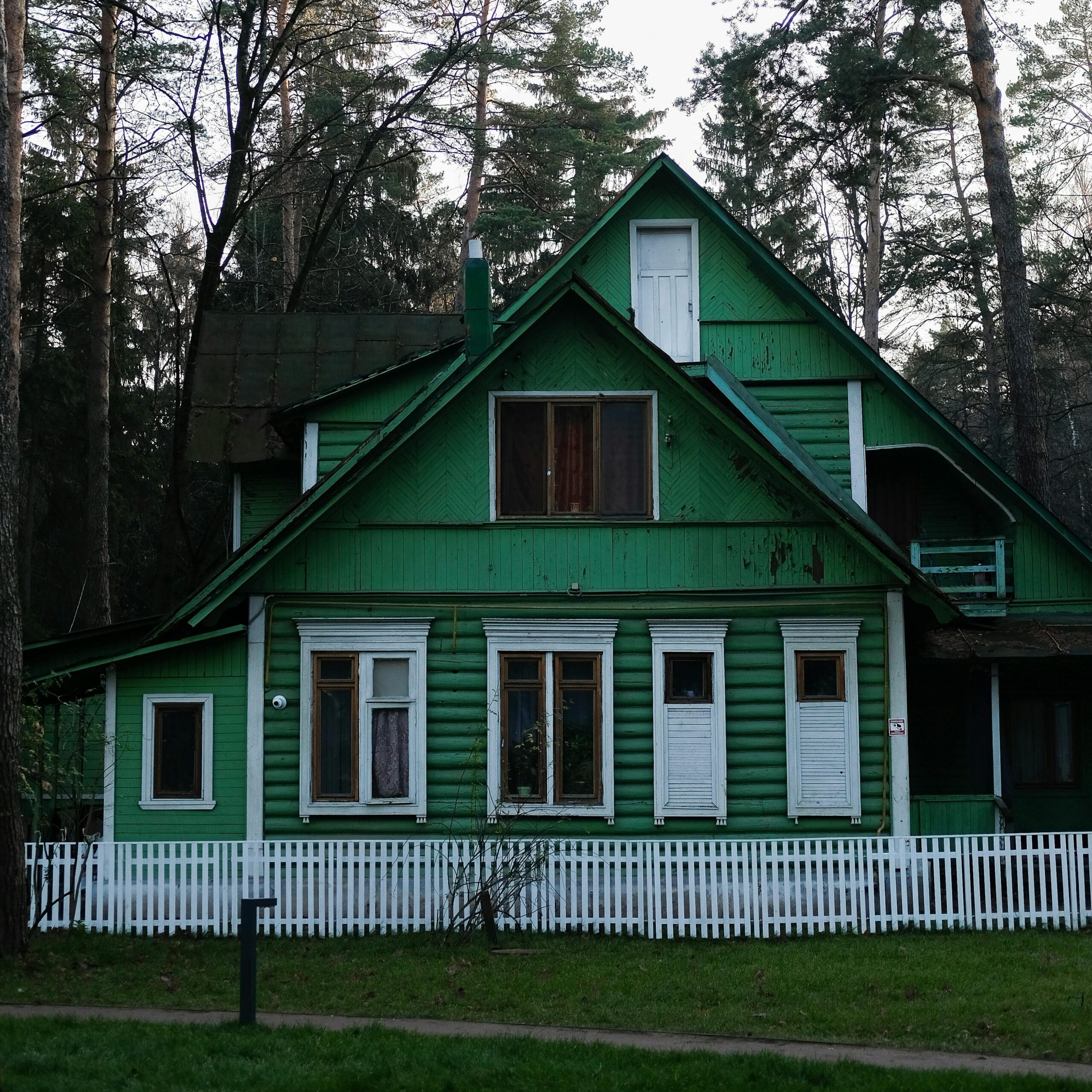 A scenic view of a green wooden house surrounded by forest in Russia.